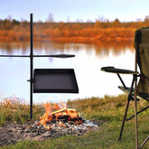 Outdoor cooking setup with a grill over a campfire by a lake
