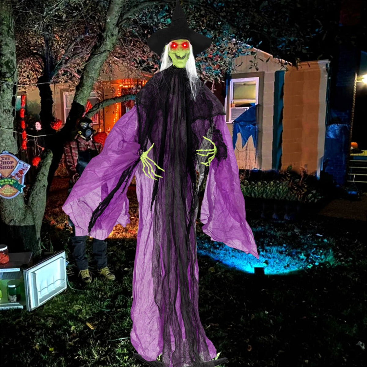 Halloween decoration of a witch with purple cape and black hat in a yard.