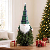Lit Christmas tree gnome on a table beside gifts and a full-size Christmas tree