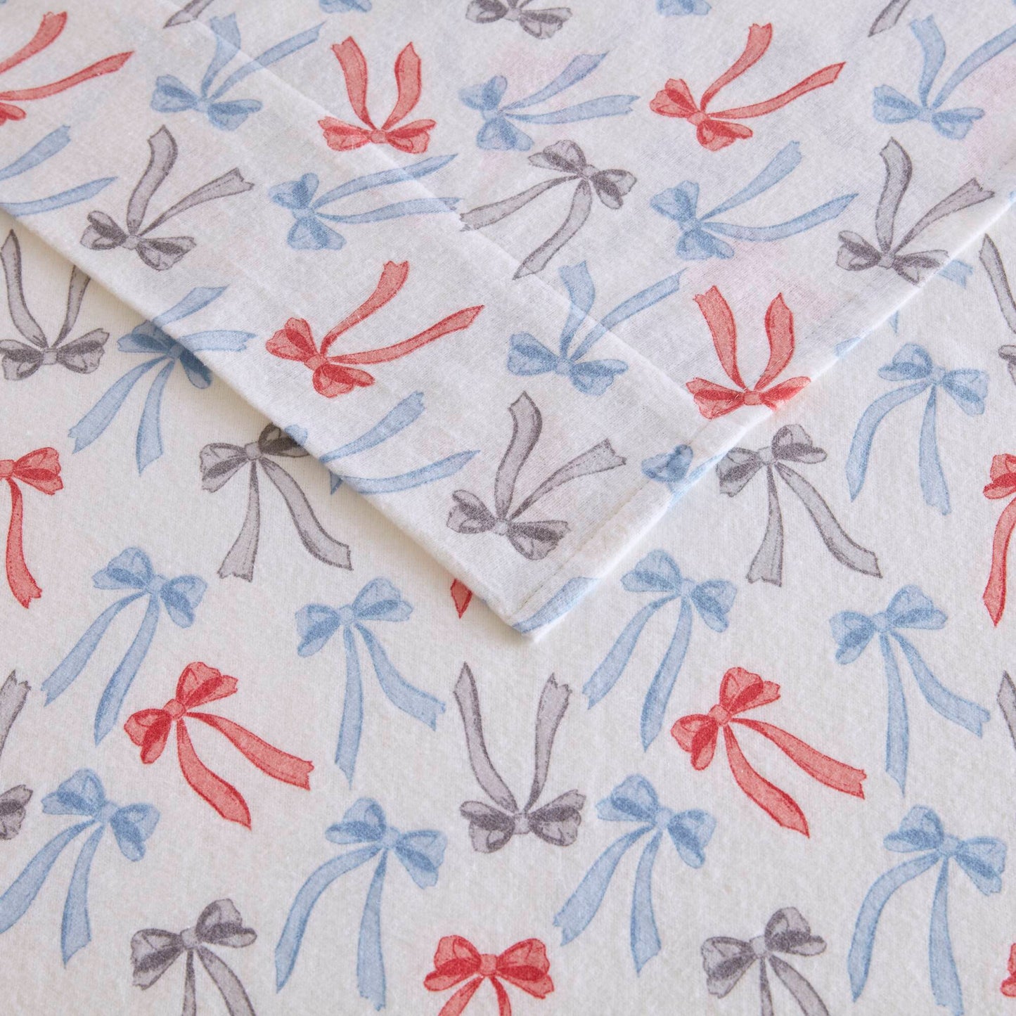 Flat lay of Happy Bows flannel sheets showing detailed bow print in red, blue, and gray on soft cotton fabric.