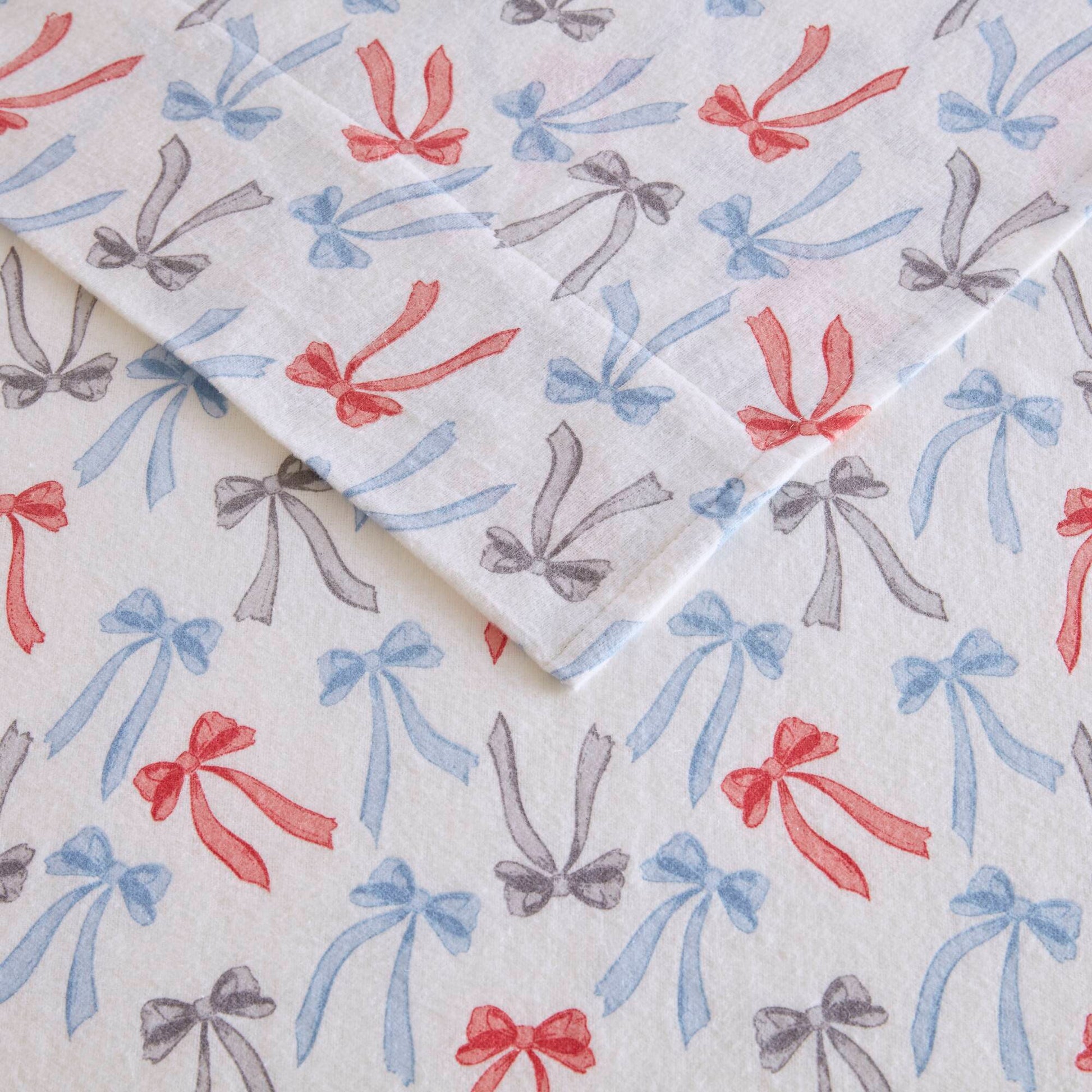 Flat lay of Happy Bows flannel sheets showing detailed bow print in red, blue, and gray on soft cotton fabric.