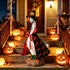 A decorative goose figurine dressed in a Halloween witch costume stands on a porch staircase surrounded by glowing jack-o&