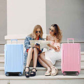 Two women sitting on steps with a blue and pink suitcase