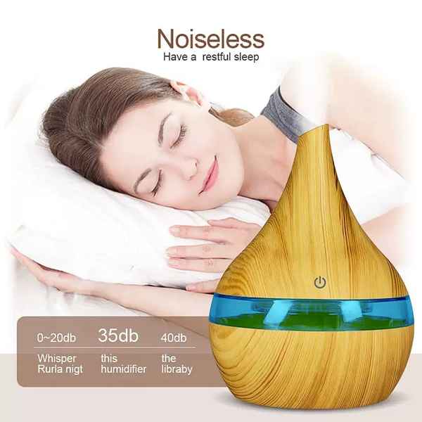 A teardrop-shaped wooden diffuser with a blue band and green liquid inside, shown in front of a sleeping woman on a white pillow. Text at the top reads &