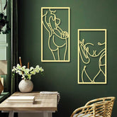 Two abstract gold line art wall decorations on a green wall with a wooden table and chair.