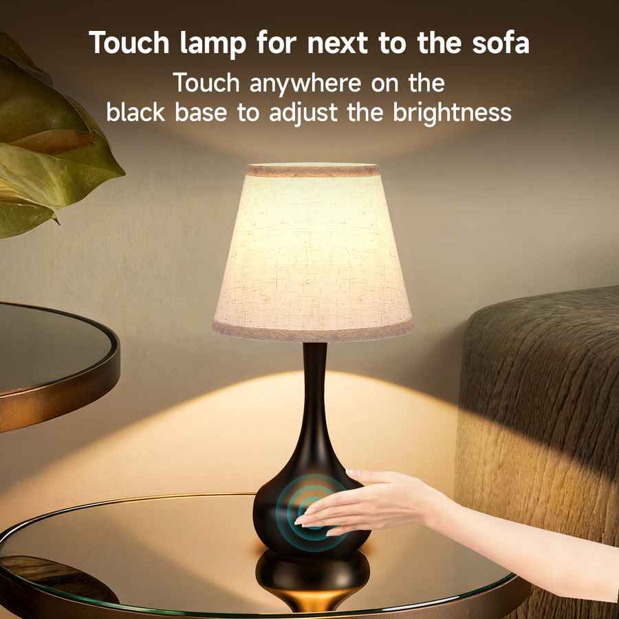 Touch lamp on a glass table with a hand interacting with it, next to a sofa.
