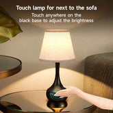 Touch lamp on a glass table with a hand interacting with it, next to a sofa.