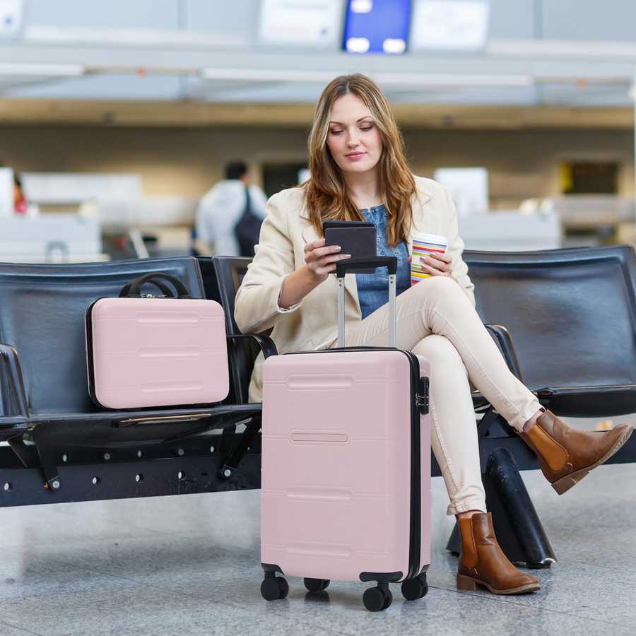 Woman sitting in an airport terminal with a pink suitcase and phone.