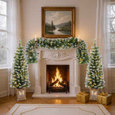 Decorated fireplace with Christmas trees and garland in a room with large windows.