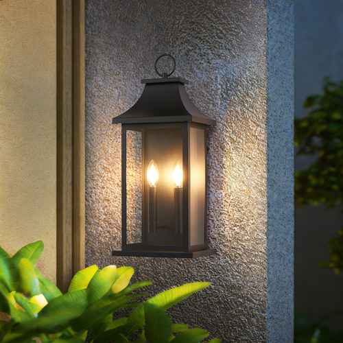 Black outdoor wall light fixture on a textured wall with plants in the foreground