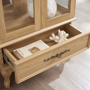 Open drawer of lighted curio cabinet showing interior storage space with decorative brass handle and wood finish.