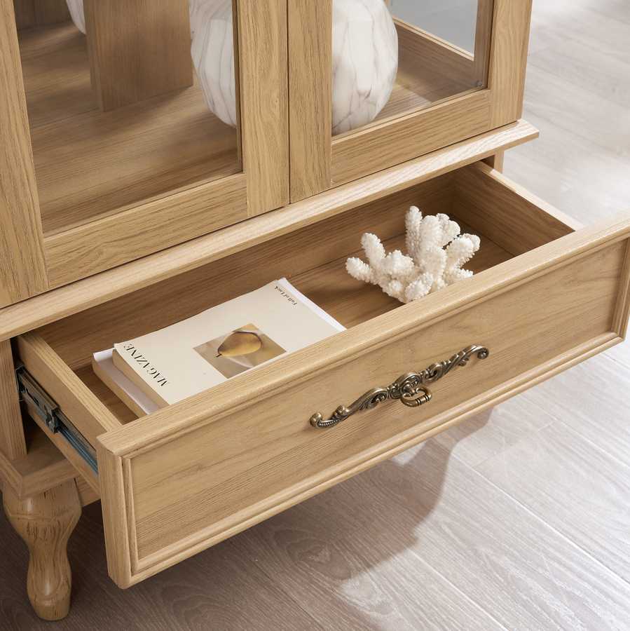 Open drawer of lighted curio cabinet showing interior storage space with decorative brass handle and wood finish.