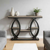 A console table with a rustic light brown wood top and shelves, supported by a black metal frame with interlocking circular arches, styled in a living room setting.