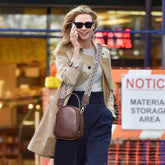 Woman in a trench coat with a brown handbag talking on a phone, blurred background