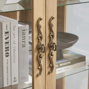 Close-up of ornate brass handles on lighted curio cabinet doors, showcasing elegant design and craftsmanship.