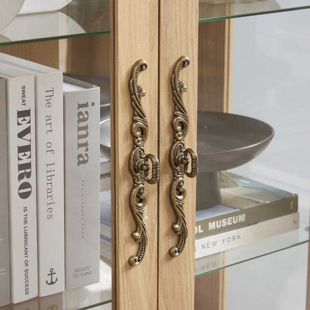 Close-up of ornate brass handles on lighted curio cabinet doors, showcasing elegant design and craftsmanship.