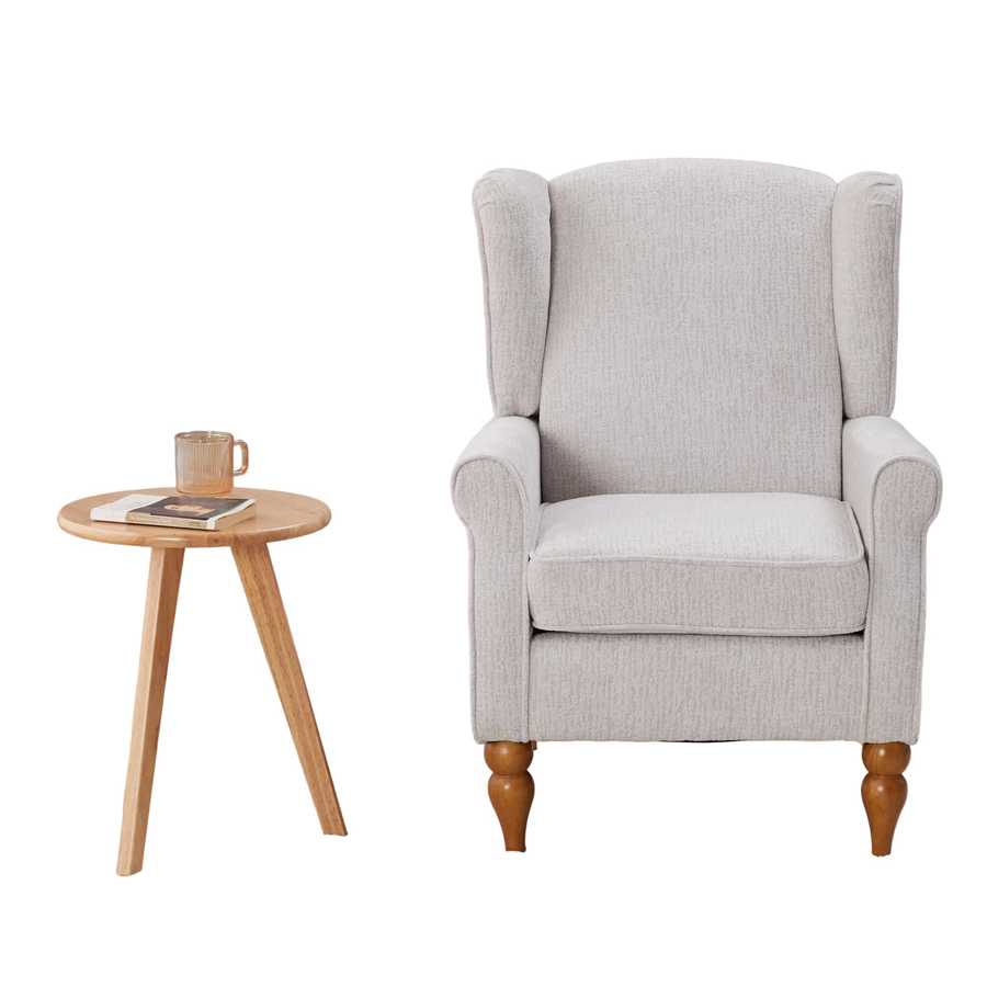 Gray armchair with wooden legs in a room with a bookshelf and small table.