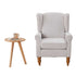 Gray armchair with wooden legs in a room with a bookshelf and small table.