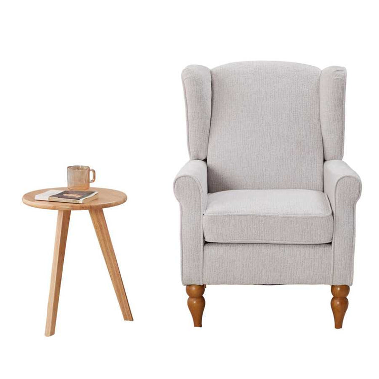 Gray armchair with wooden legs in a room with a bookshelf and small table.
