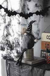 Halloween display with black gnome and other spooky decorations, including a black tree, ghost, and gnome figures with witch hats, on a decorated table.