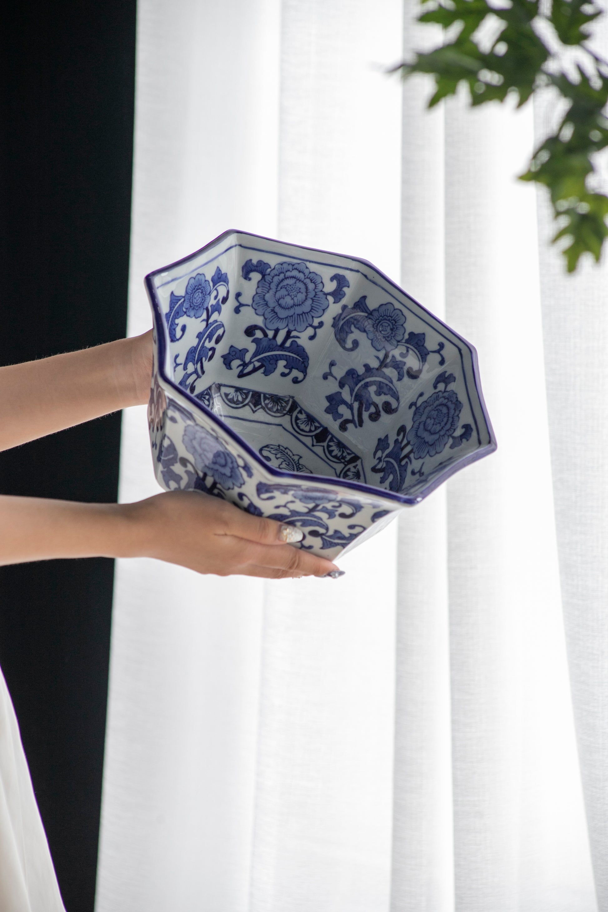 Blue and White Decorative Bowl - Porcelain, Elegant Design held by hands near a white curtain, showcasing its floral interior pattern.