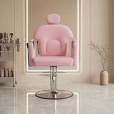 A pink salon chair with a rounded, cushioned design and chrome base, positioned in front of a backlit mirror in a modern, beige-toned salon interior.