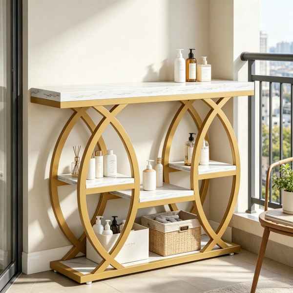 A modern console table with a white marble-look top and shelves, supported by large interlocking gold-tone circular metal frames. The table is styled with toiletry bottles and a wicker basket, set in a bright room with a balcony view.
