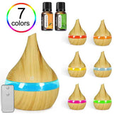 A wooden diffuser lamp with a blue light band shown prominently, alongside smaller variants with orange, yellow, light blue, pink, and green bands. Two small essential oil bottles labeled Henley are shown at the top, a rainbow &