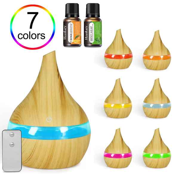 A wooden diffuser lamp with a blue light band shown prominently, alongside smaller variants with orange, yellow, light blue, pink, and green bands. Two small essential oil bottles labeled Henley are shown at the top, a rainbow &