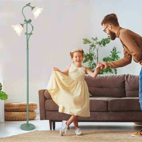 Child in a yellow dress being helped by an adult in a living room with a green floor lamp and brown sofa.