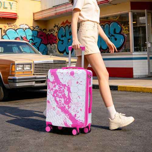 Person walking with pink printed spinner luggage set in front of colorful graffiti wall, holding handle, wearing beige shorts and white sneakers