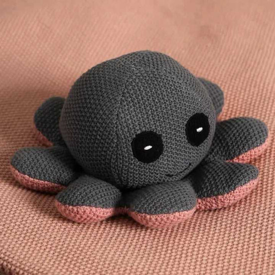 Knitted octopus plush toy with black eyes and pink accents on soft textured fabric