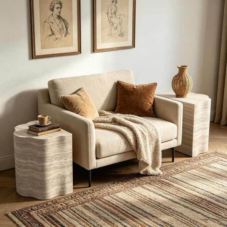 Living room with beige sofa, framed artwork, textured side table with a vase, books, and a cozy blanket