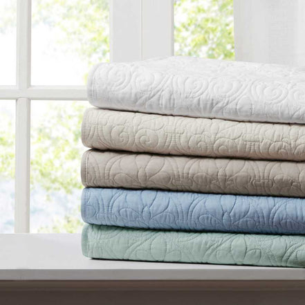 Stack of oversized quilted throws in multiple colors including white, beige, and blue, ideal for home bedding comfort and style.