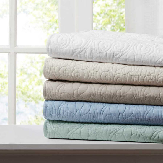 Stack of oversized quilted throws in multiple colors including white, beige, and blue, ideal for home bedding comfort and style.