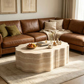 Living room with brown leather sofa, beige pillows, cozy blanket, and a marble coffee table with decorative items, in a warm, inviting space.