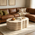 Living room with brown leather sofa, beige pillows, cozy blanket, and a marble coffee table with decorative items, in a warm, inviting space.