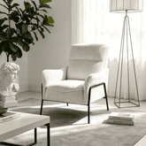 A cream ribbed fabric armchair with black metal legs, styled in a bright, modern living room next to a white coffee table, a floor lamp, and a potted plant.