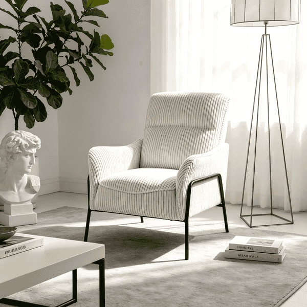 A cream ribbed fabric armchair with black metal legs, styled in a bright, modern living room next to a white coffee table, a floor lamp, and a potted plant.