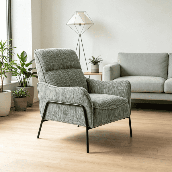 A modern upholstered accent chair in a textured sage green fabric with black metal legs, set in a bright, contemporary living room next to a light gray sofa and potted plants.