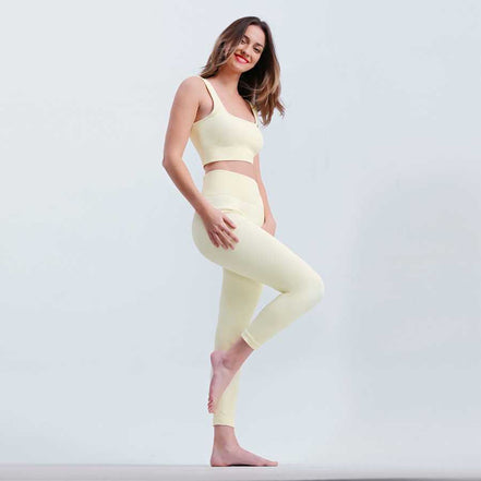 Woman wearing a light yellow sports bra and leggings on a white background
