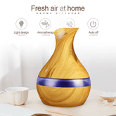 Wood grain aroma diffuser with a purple band, shown on a tabletop with small cups and text overlays highlighting features like light design, aromatherapy, silent operation, and auto off.