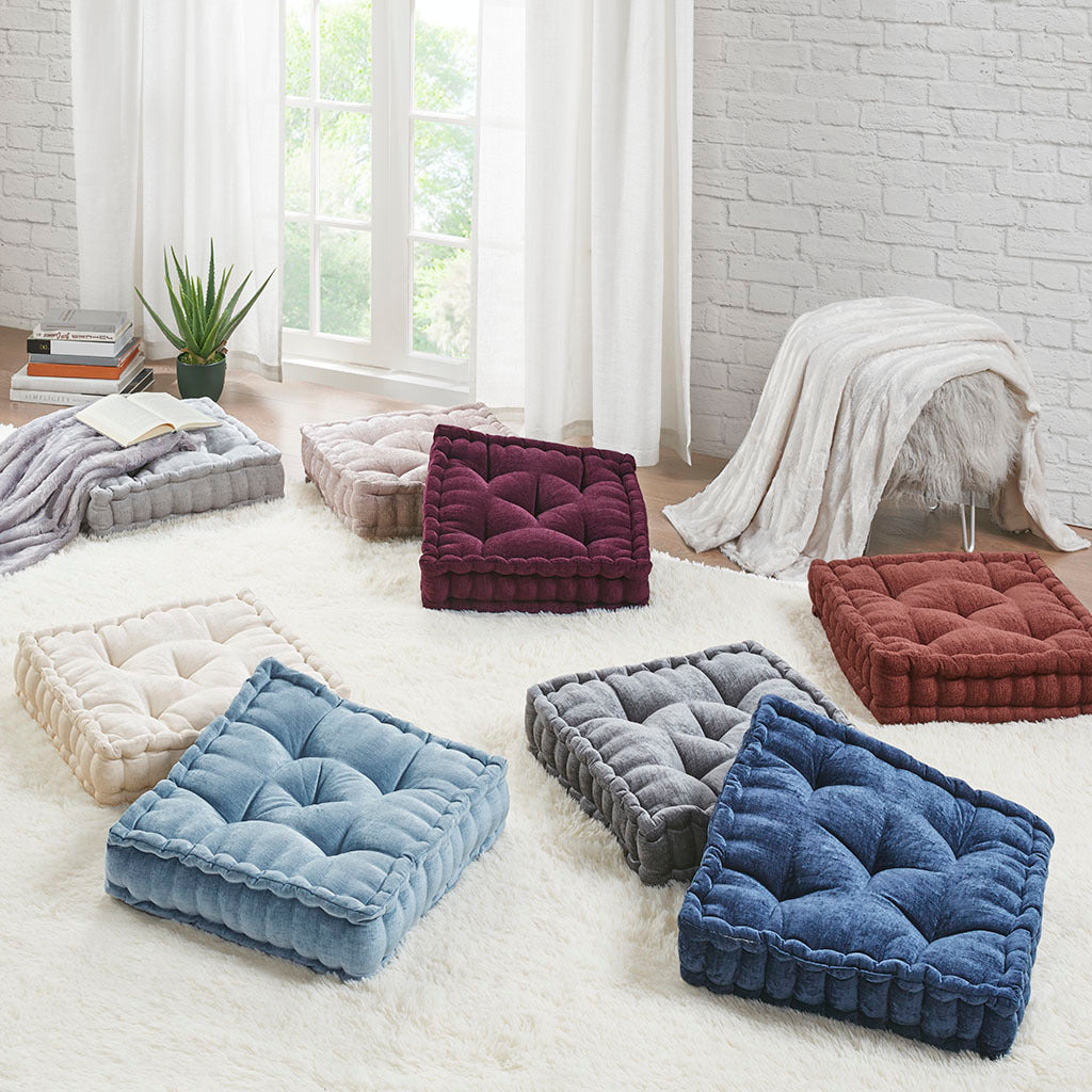 Colorful floor cushions on a light-colored rug in a room with white brick walls and large windows.