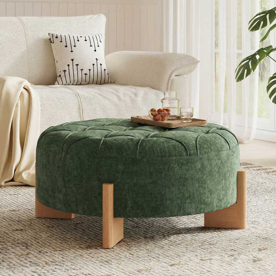 Green ottoman in front of a beige armchair with a decorative pillow in a living room setting.