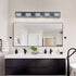 Bathroom vanity with mirror, lights, and various items on a neutral wall.