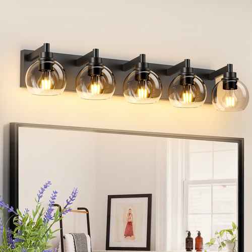 A five-light bathroom vanity wall sconce with a matte black metal frame and clear glass shades, mounted above a mirror in a bright room.
