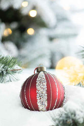 Red Christmas ornament with white snowflake pattern on a snowy background