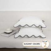 Set of two decorative pillows with ruffled edges on a bed, labeled &