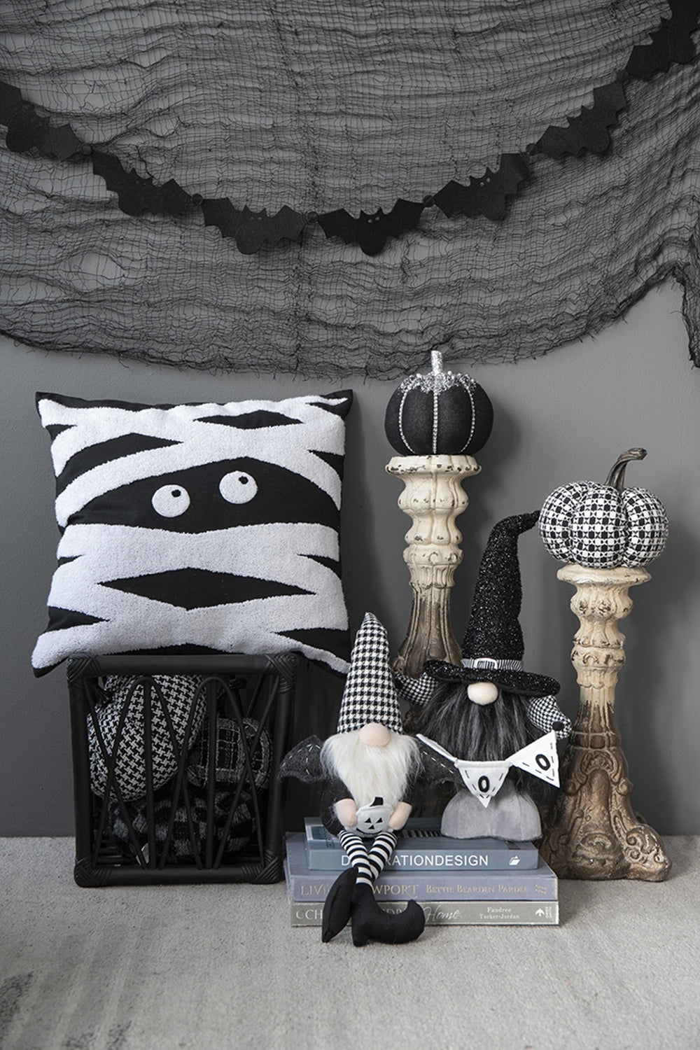 Halloween-themed decor with mummy pillow, gnomes, and pumpkins against a gray wall.