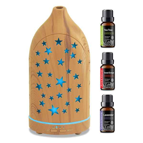 A wooden diffuser with blue star-shaped light cutouts and a blue mist spray base, shown alongside three essential oil bottles labeled Tea Tree, Sweet Orange, and Lavender on a white background.